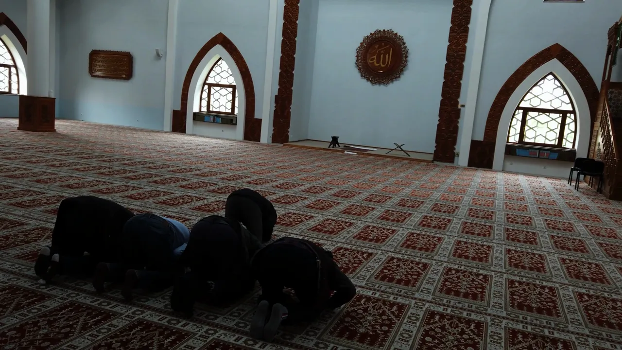 Interior of a mosque with patterned carpet and worshippers in prayer