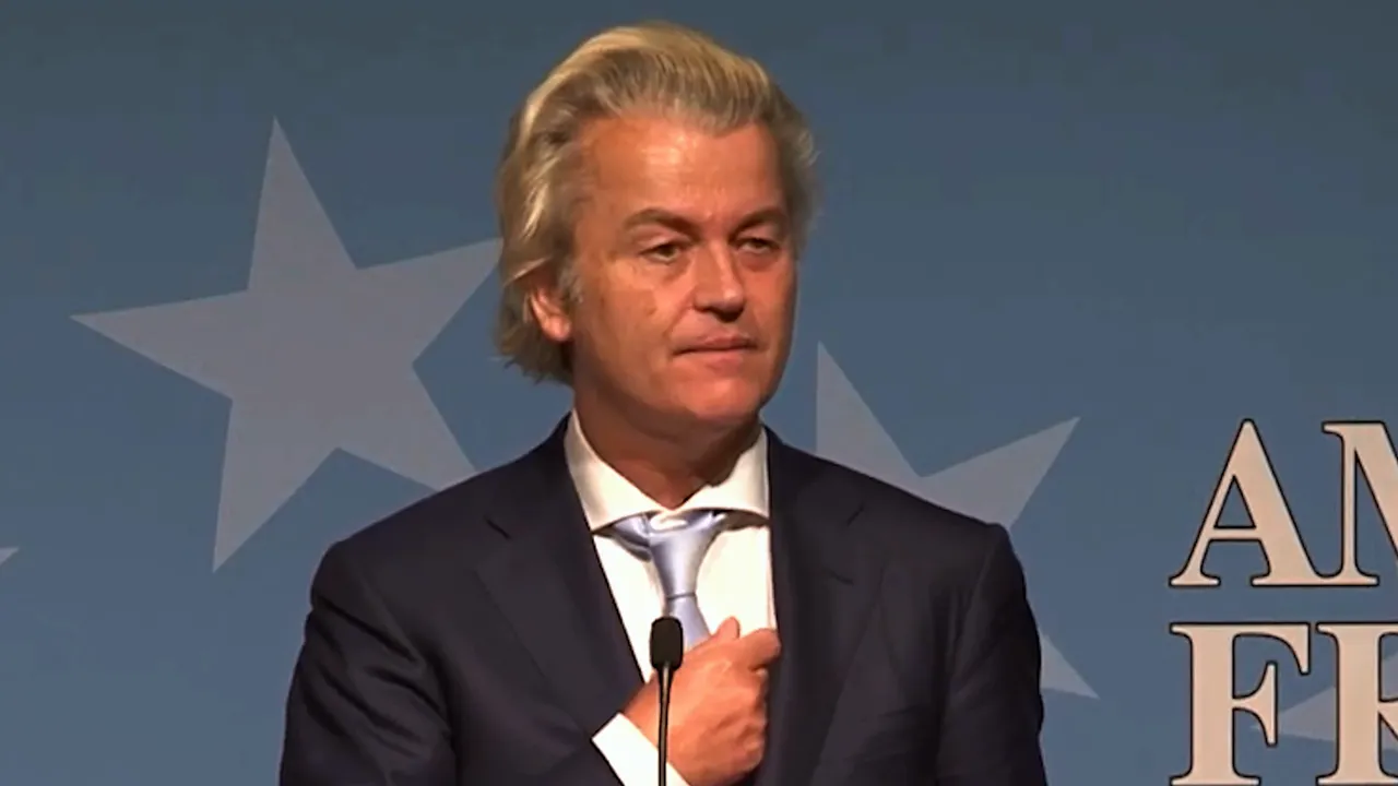Male speaker at a podium adjusting his tie, with a blue backdrop featuring star shapes