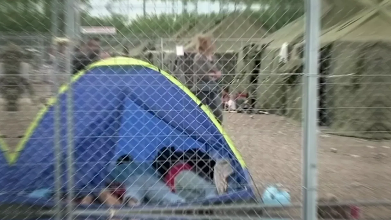 Tent and people behind a chain-link fence at a migrant reception site