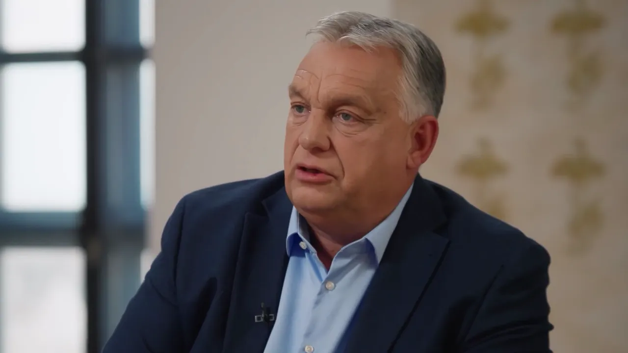 Political leader speaking in a studio interview, mid-shot with suit and blurred background