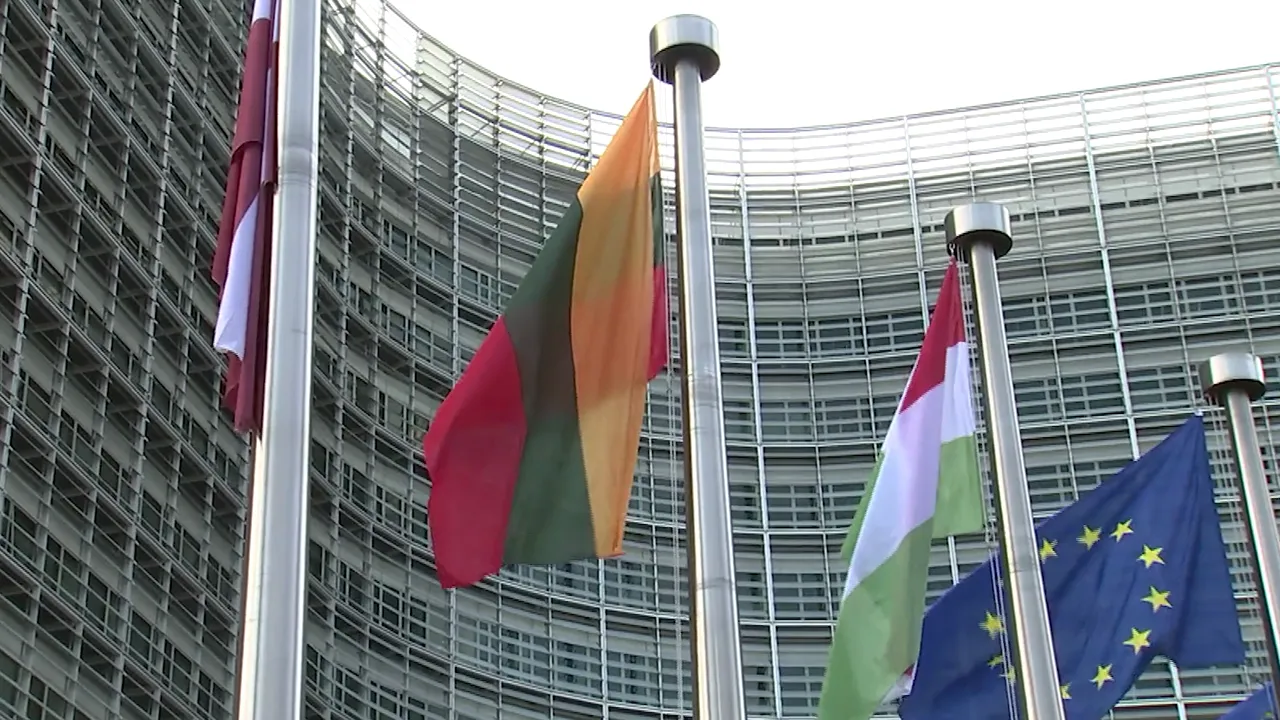 National flags and the European Union flag flying in front of a modern EU institutional building.