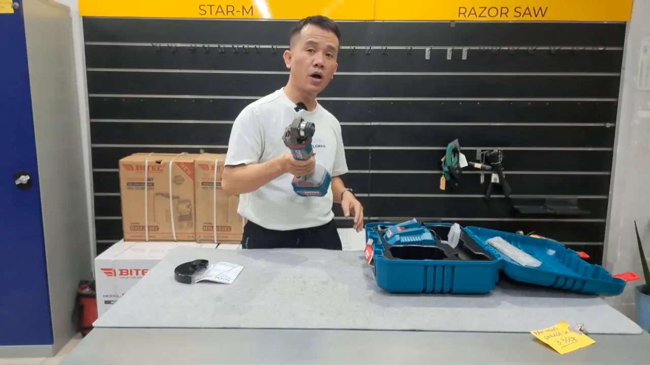 Người giới thiệu giơ máy mài góc Total TAGLI4128102 về phía máy quay, làm rõ đầu máy, thân và pin.