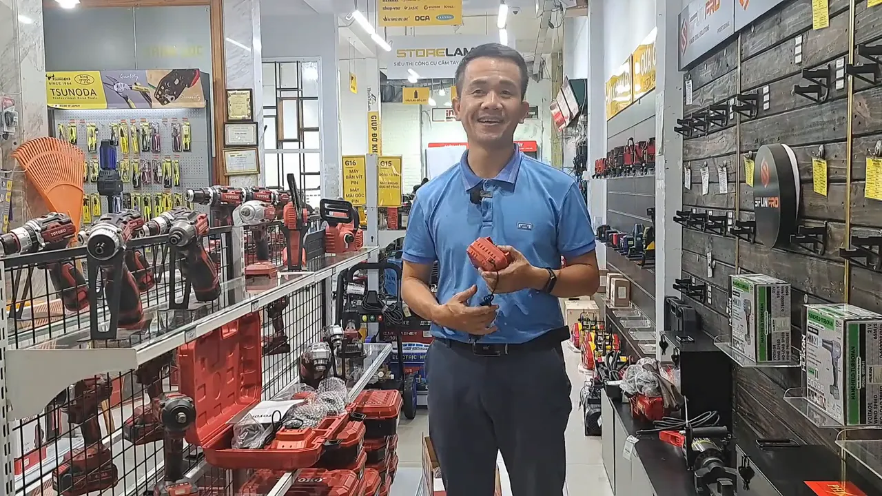 Người đứng chính diện cầm viên pin đỏ trước kệ dụng cụ, rõ nét và sáng