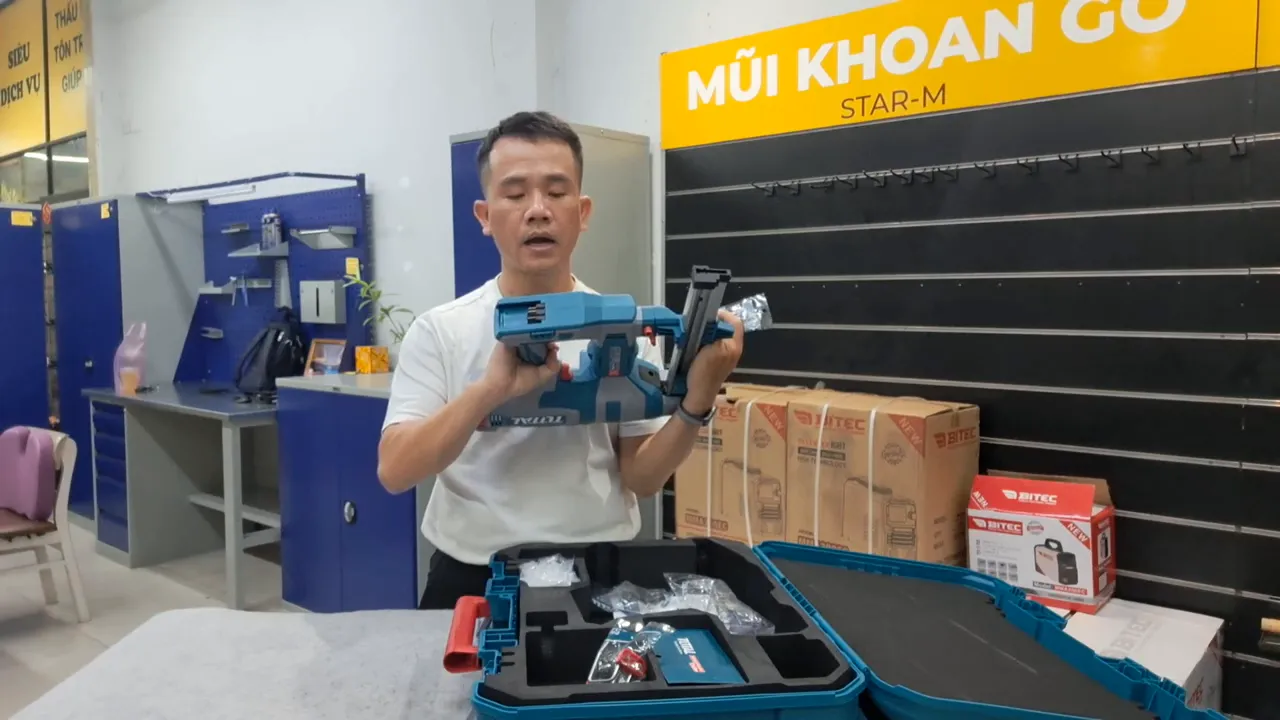 Người cầm máy bắn đinh Total, đồng thời cầm túi phụ kiện nhỏ chứa đầu bơm/đầu chuyển khí