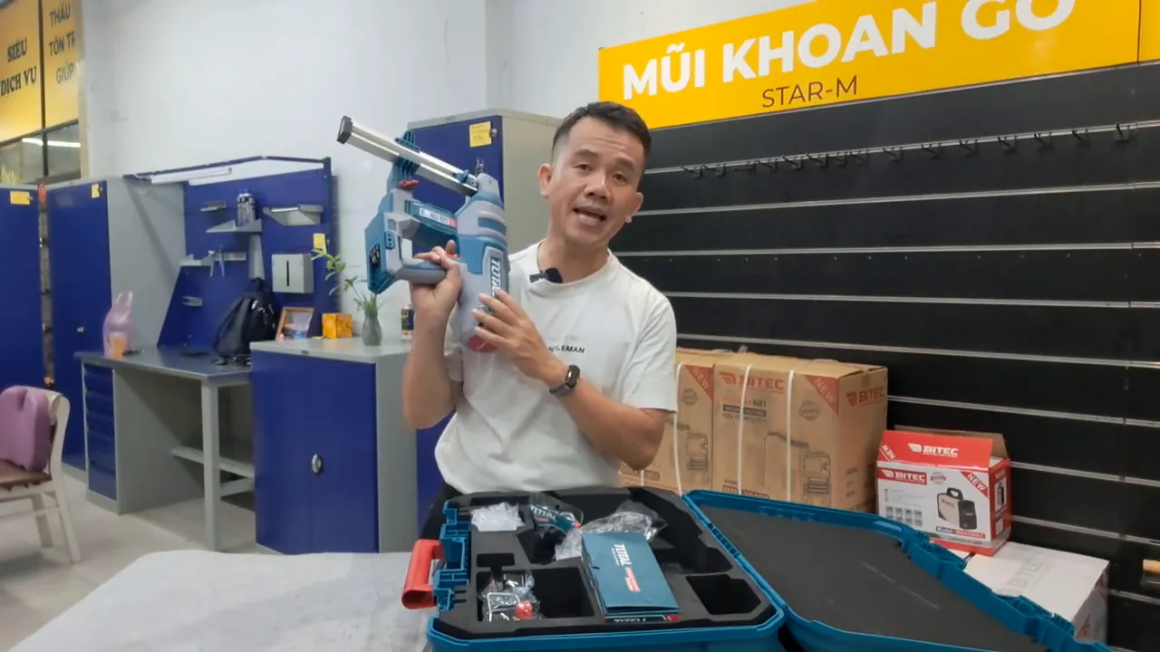 Máy bắn đinh Total TCNLI420602 được cầm lên, hiển thị rõ thân, đầu bắn và hộp phụ kiện