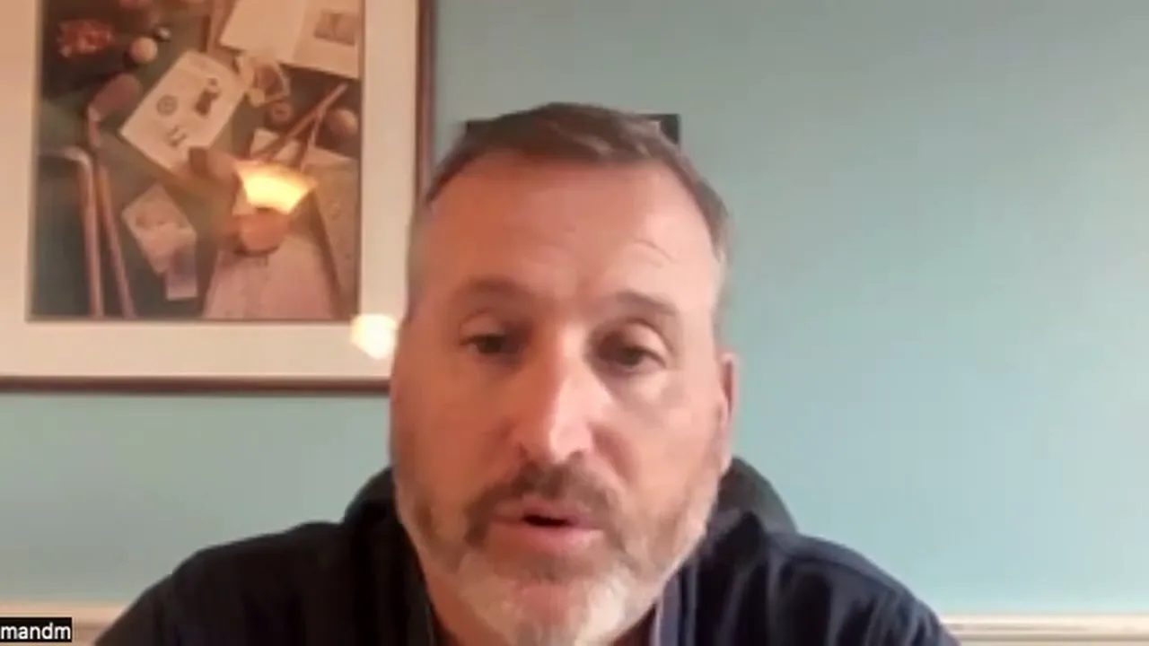 Clear frontal video-call screenshot of a presenter discussing switching processors and equipment lock-in with a teal wall and framed art behind him.