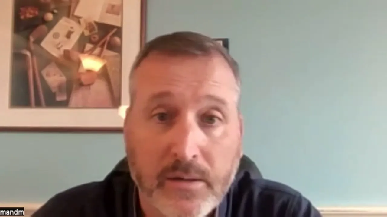 Clear frontal video-call screenshot of a presenter addressing funding holds with teal background and framed picture