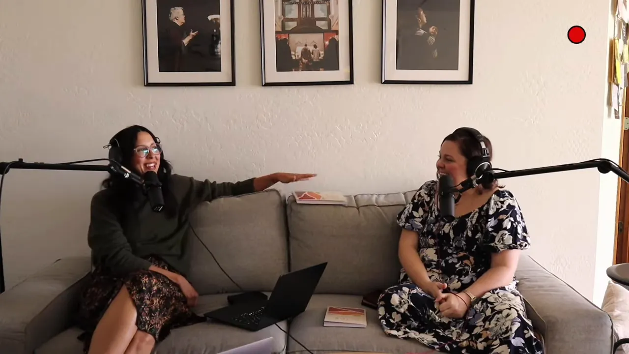 Two hosts on a couch with microphones and headphones, a devotional book centered between them while one gestures over it.