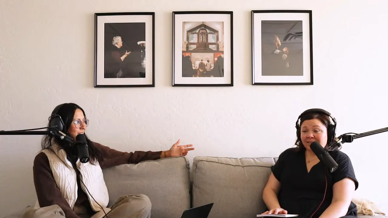 Two hosts talking into microphones on a couch with framed photos on the wall behind them, podcast recording setup visible.