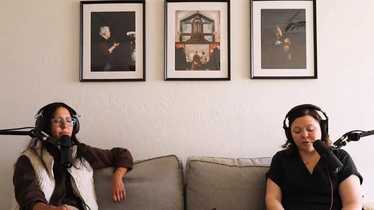 Podcast host speaking into a microphone with headphones on while a co‑host listens on a couch, well lit and clear.
