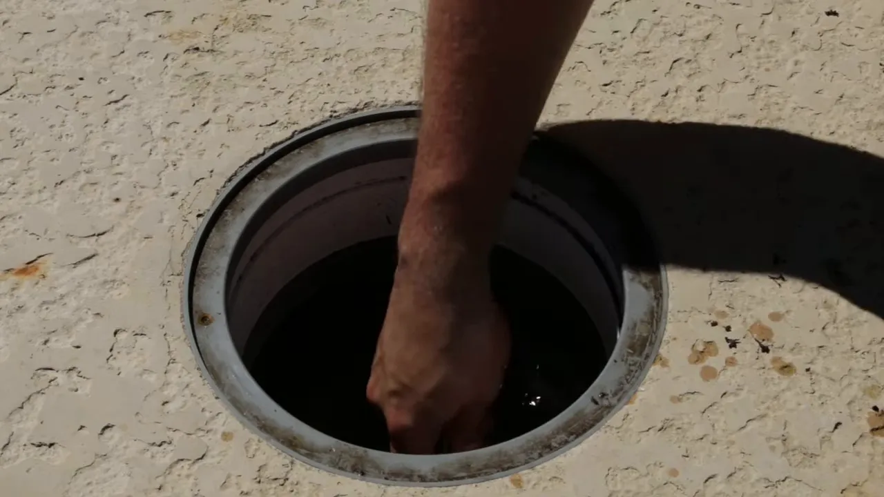 A hand reaching down into an open pool skimmer to remove the basket.