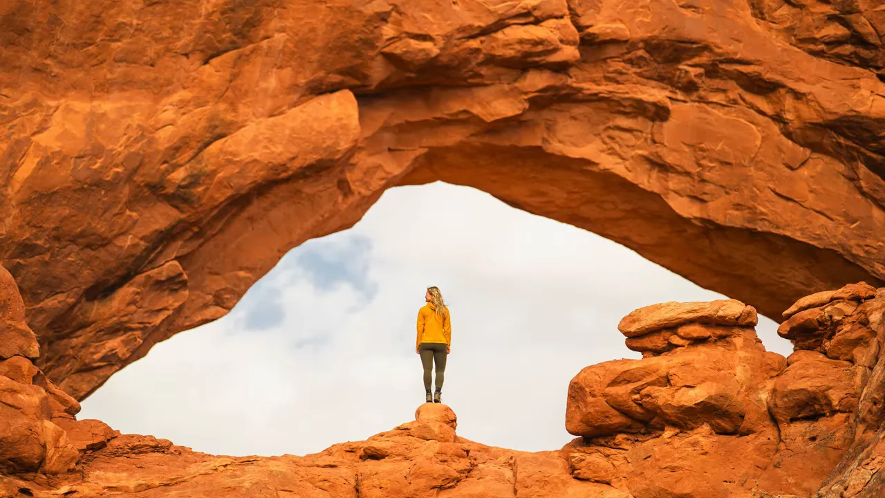 Person standing beneath a sandstone arch at Arches National Park, illustrating scale and easy access