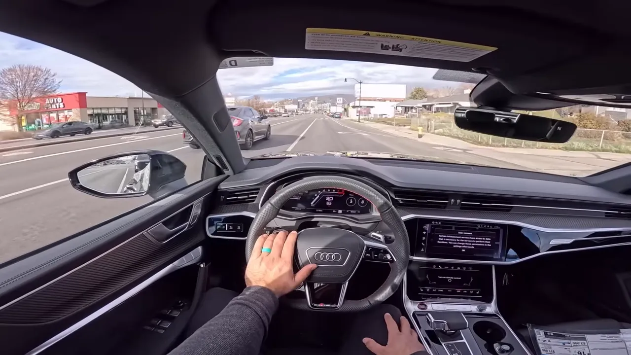 Wide driver POV of Audi RS7 interior with steering wheel, digital gauge cluster, dual touch screens and clear view of the road ahead