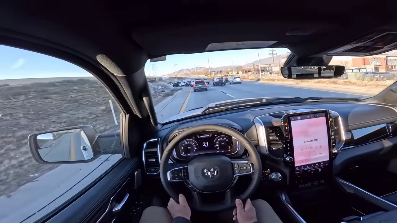 Ram 1500 cockpit view showing steering wheel, digital gauge cluster reading 21 mph, center touchscreen and traffic ahead