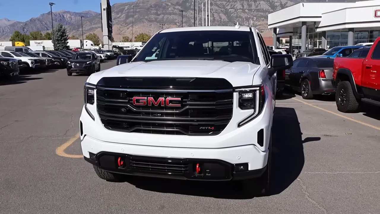 Full front view of 2026 GMC Sierra 1500 AT4 in white emphasizing black grille, headlight bezels and red recovery hooks