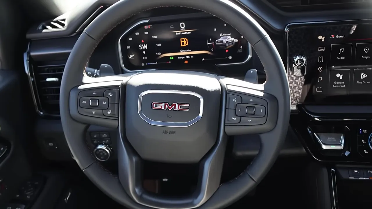 Driver's view of GMC steering wheel with the digital instrument cluster visible behind it and the center infotainment screen at the right