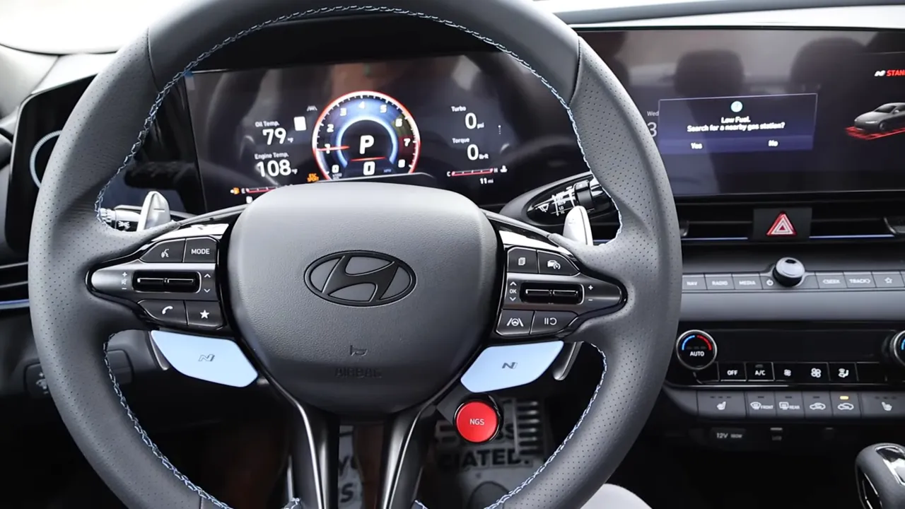 close-up Hyundai Elantra N steering wheel showing perforated rim, paddle shifters and red NGS button with digital gauges