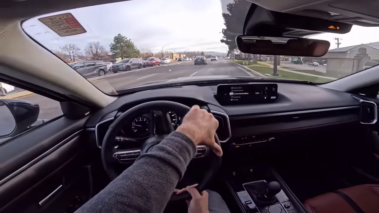 Forward interior view of Mazda CX-50 cruising with infotainment screen and relaxed steering