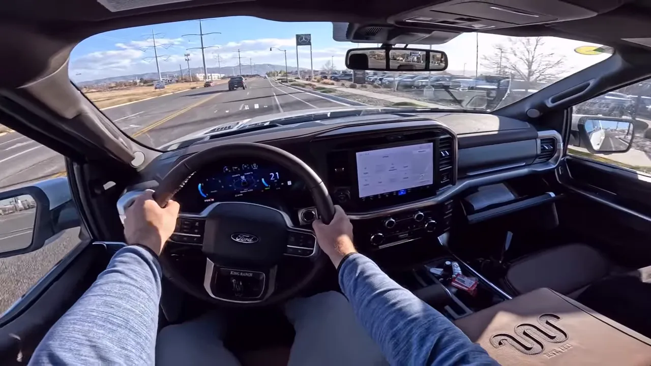 Driver POV inside 2026 Ford F-150 King Ranch showing steering wheel, instrument cluster and center touchscreen while driving down the road