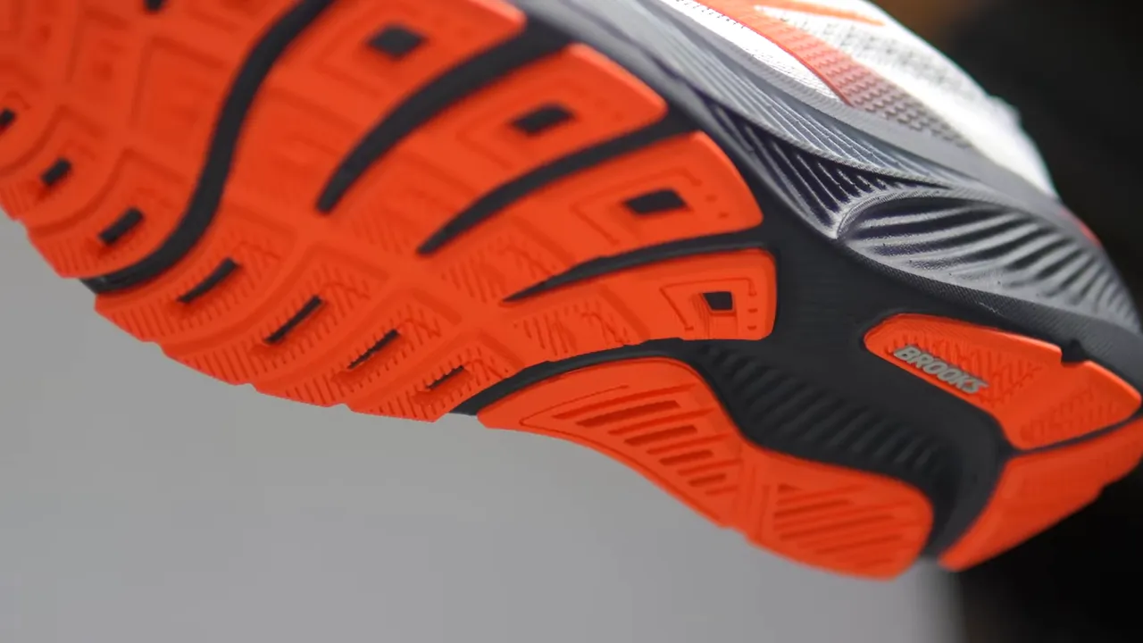 Underside view of Brooks Ghost 17 showing orange segmented outsole with cross-cut flex grooves and midfoot sculpting