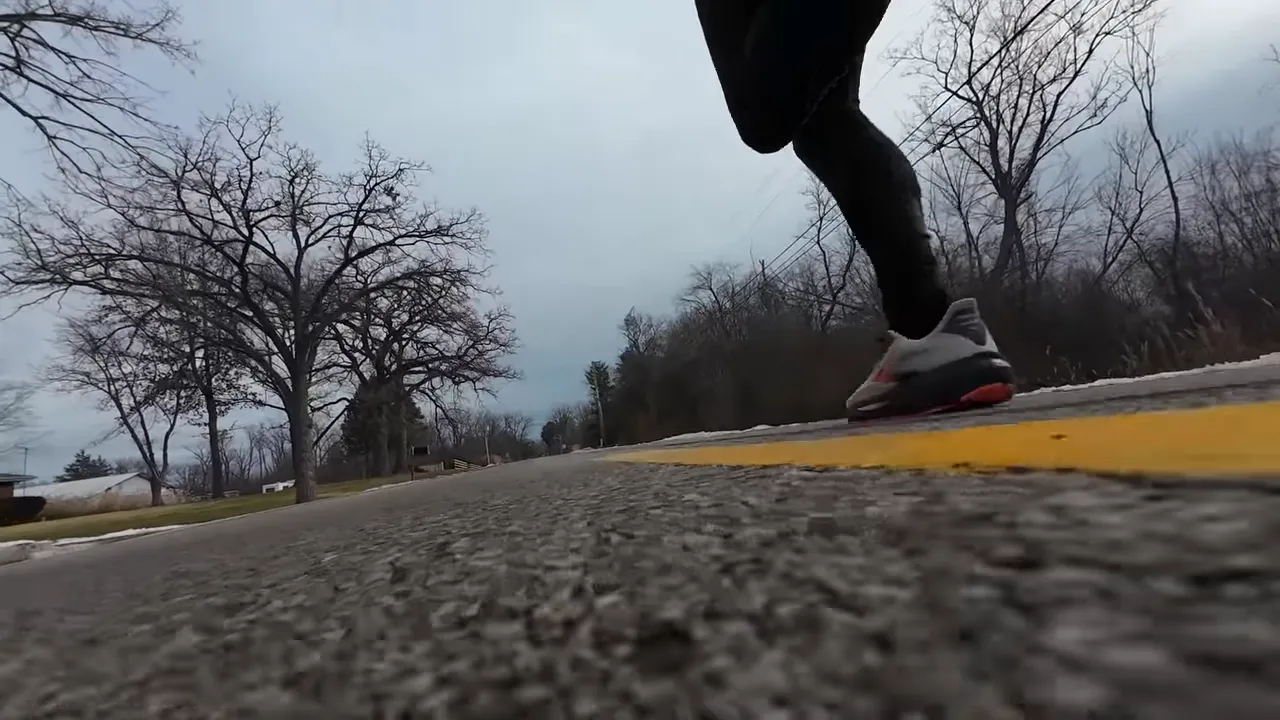 Low-angle running shot of a Brooks Ghost 17 mid-stride on an asphalt road showing the outsole and toe-off