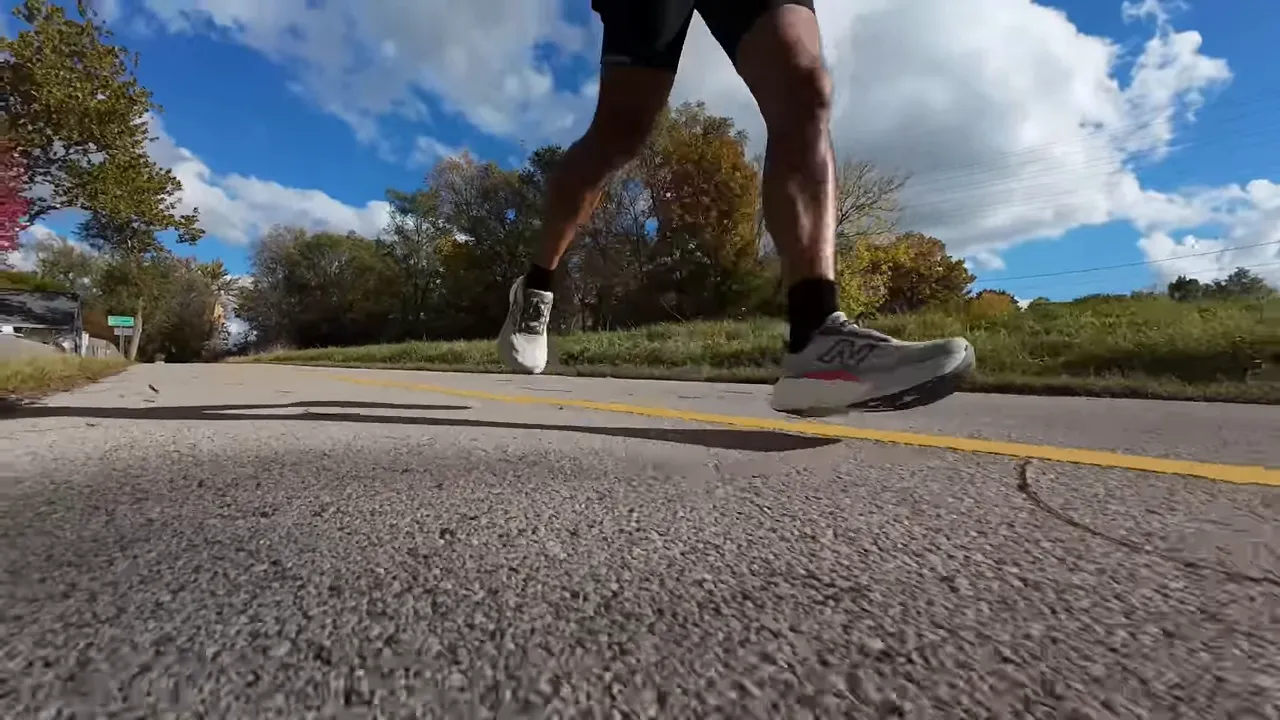 Runner mid-stride on a road showing the lateral profile of the New Balance Fresh Foam X More v6, highlighting the thick midsole and slightly curved rocker