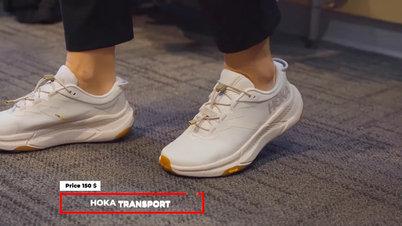 Pair of white Hoka Transport walking shoes on carpet with on-screen HOKA TRANSPORT title.
