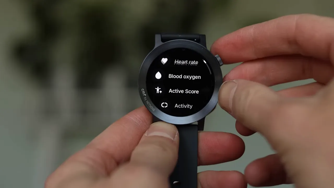 Close-up of the CMF Watch 3 Pro showing Health menu items (Heart rate, Blood oxygen, Active Score) while the crown is being adjusted.