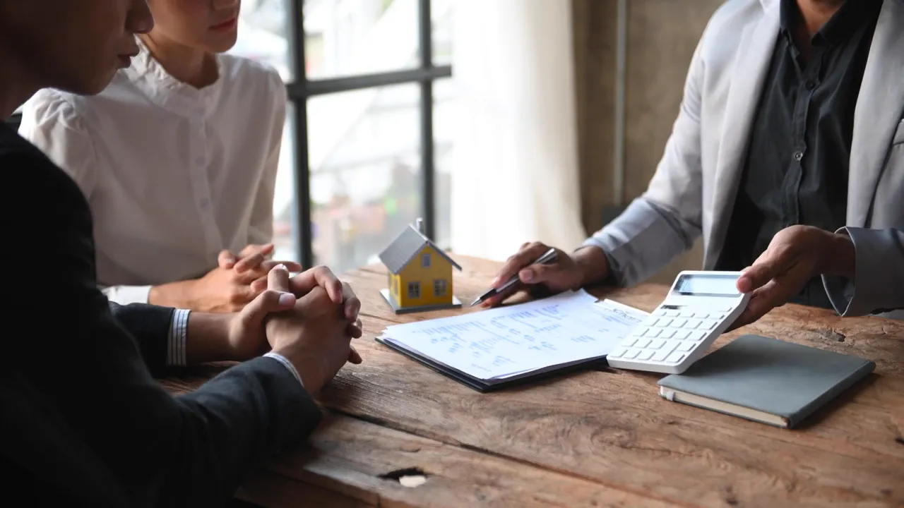 Advisor showing a calculator and papers across from clients with a small house model on the table