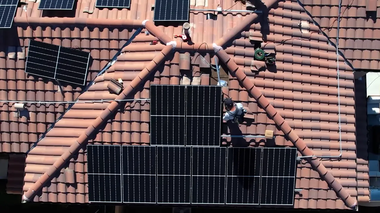 Aerial view of rooftop solar panels being installed on a tiled roof with an installer at work