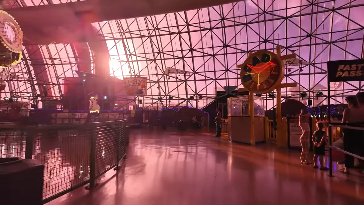 Indoor amusement dome with rides, neon signage and open floor area with a family waiting in line