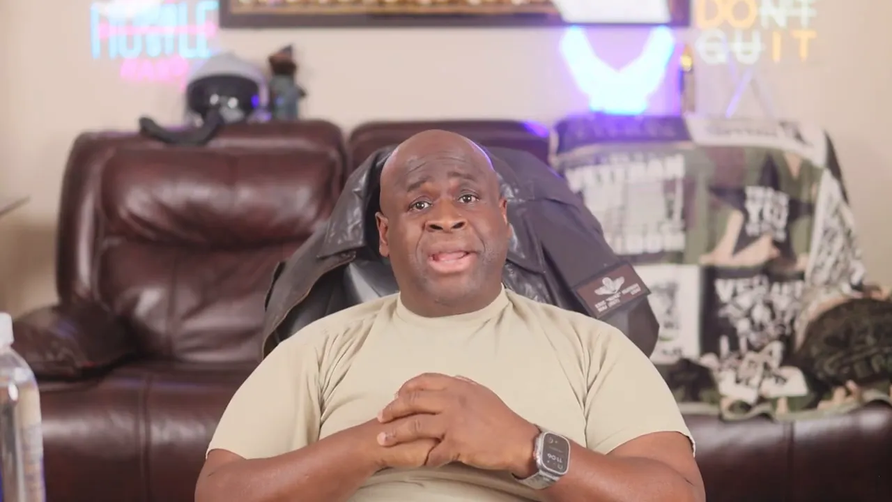 Presenter seated, hands clasped, speaking directly to camera in a home setting.