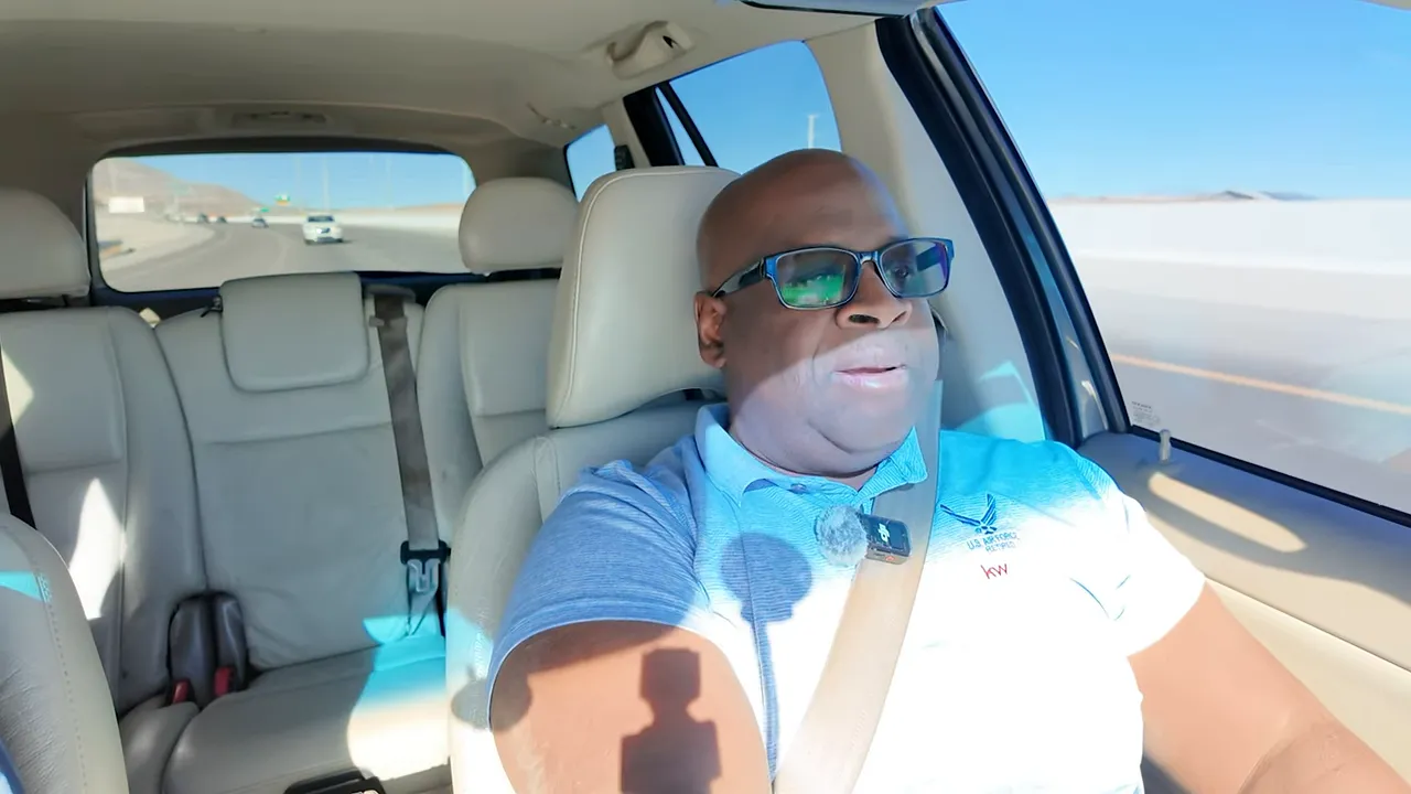 Host speaking while driving in a car, well-lit wide shot showing the interior and highway outside.