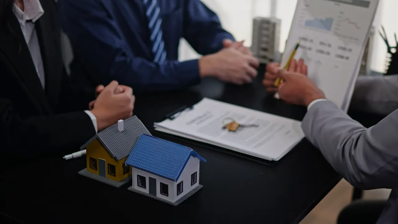 Two small house models next to a contract with keys on a table during a negotiation