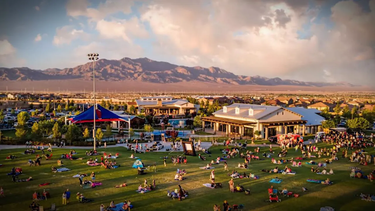 Wide view of a park and community hub with many families on the lawn, pools and mountains in the background.