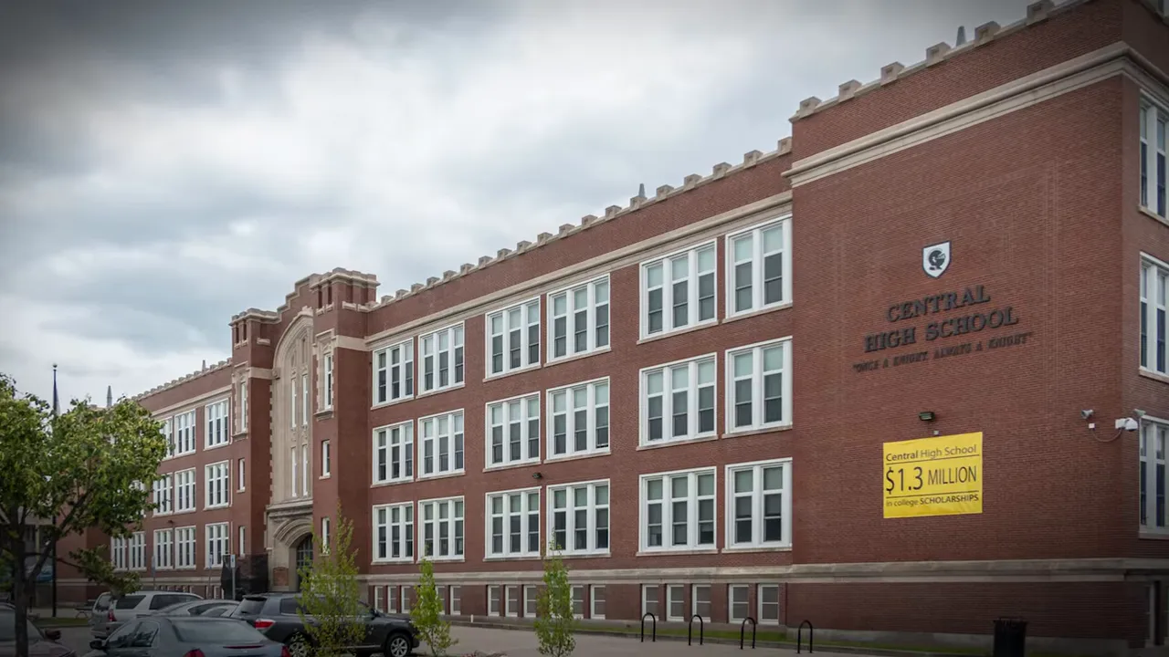Red brick multi-story high school building exterior with many windows and parked cars