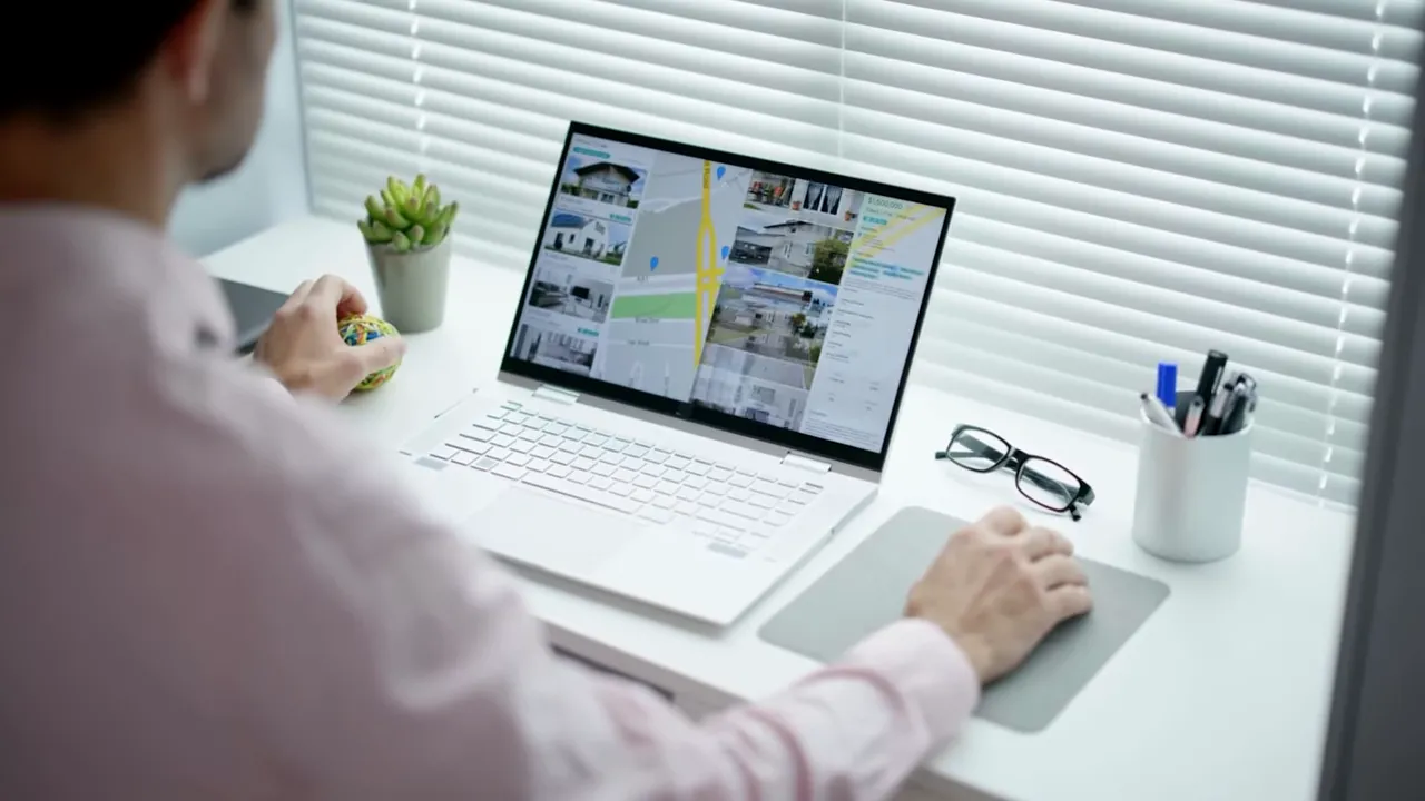 Workspace laptop displaying property listings and map, glasses and pen cup beside it