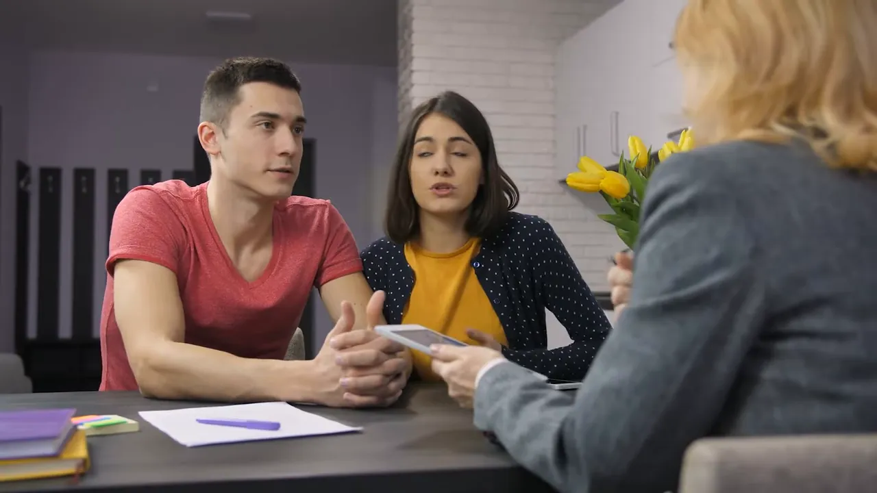 Couple talking with an agent across a desk while reviewing documents or a tablet
