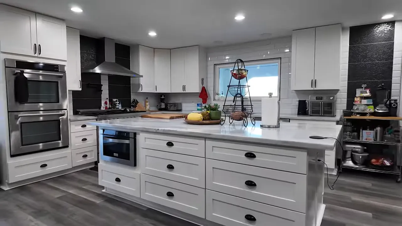 White chef's kitchen with large marble island, built-in drawers and double oven