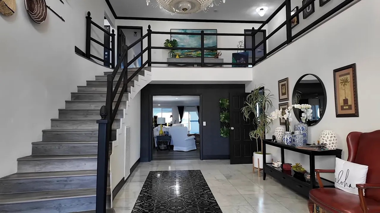 Wide foyer showing the staircase rising to an open upstairs balcony, foyer table, tiled floor and entryway beyond.