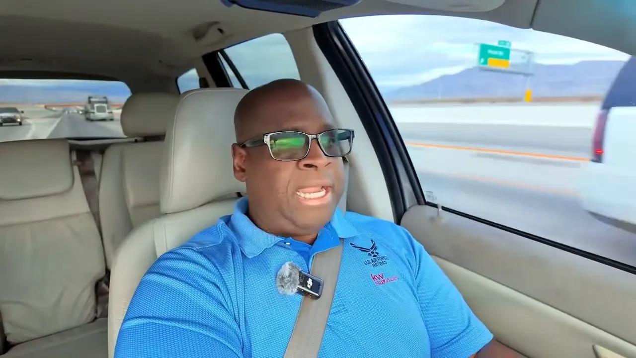 Person in blue polo driving with highway exit sign visible through the window, speaking to camera