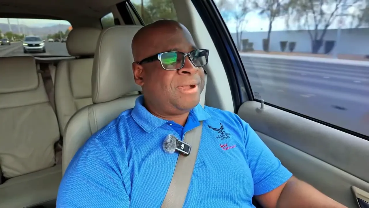 Person in blue US Air Force Retired polo driving a car, clear view of clip-on microphone and outside street scene