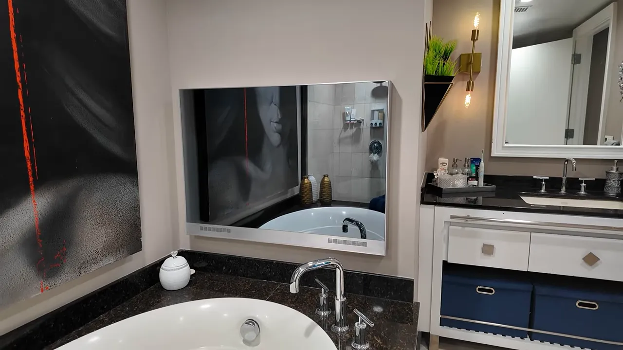 Owner's bathroom showing a jetted bathtub with dark stone surround, chrome faucet and a built-in mirror TV on the wall