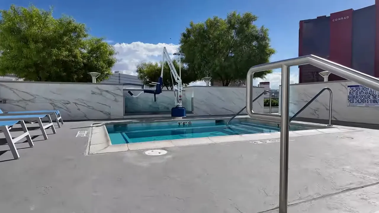 Outdoor pool at Sky Las Vegas with a visible pool lift chair, shallow spa section, handrails, and lounge chairs on the deck.