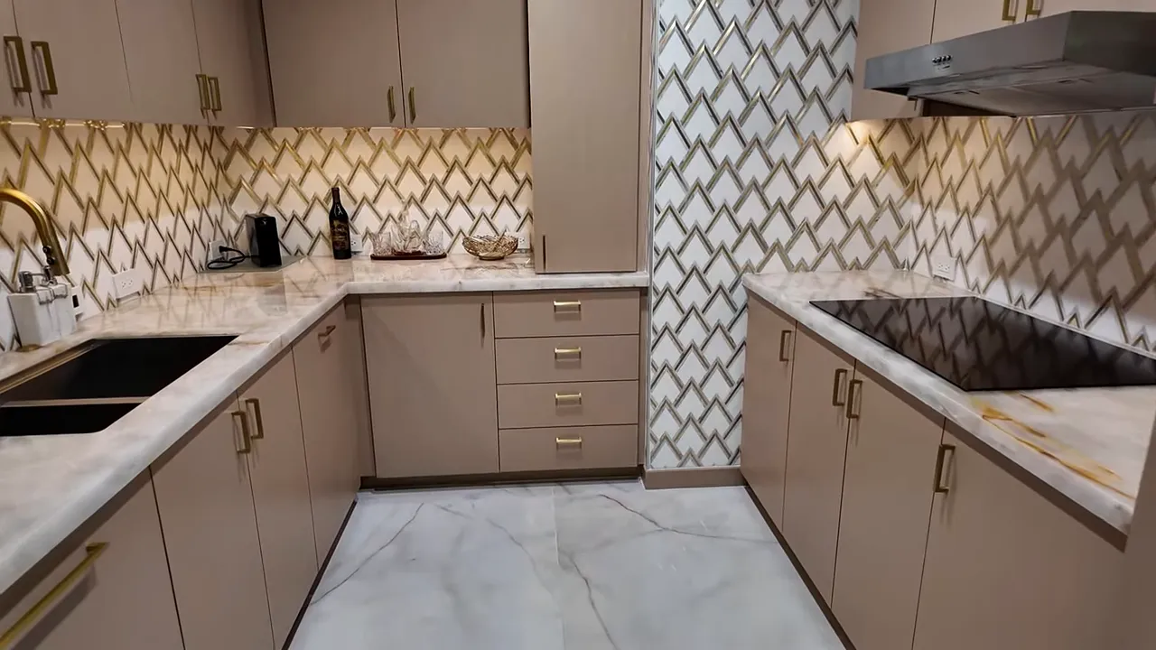 Well-lit kitchen showing marble countertops, patterned backsplash, sink, and induction cooktop.