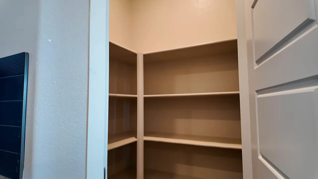 Walk-in kitchen pantry with built-in corner shelves and open white door