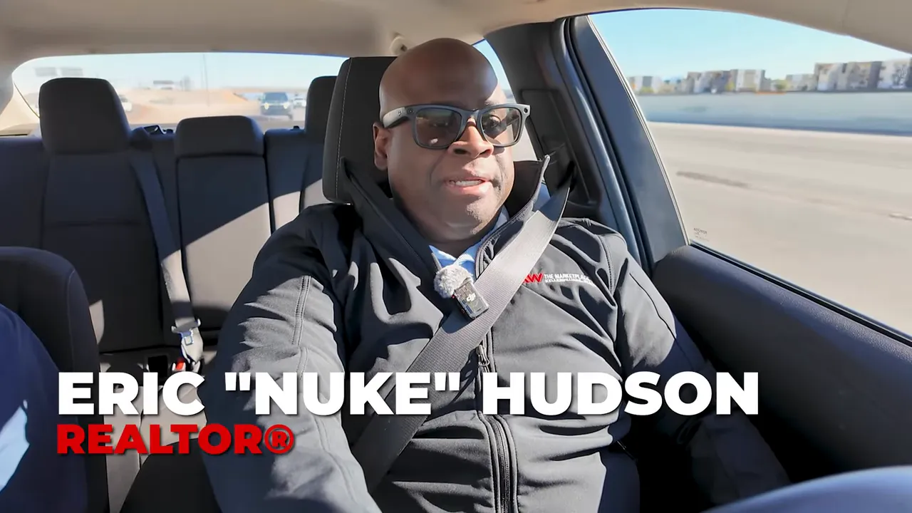 Presenter seated in a car speaking to camera with a name/branding overlay in the frame.