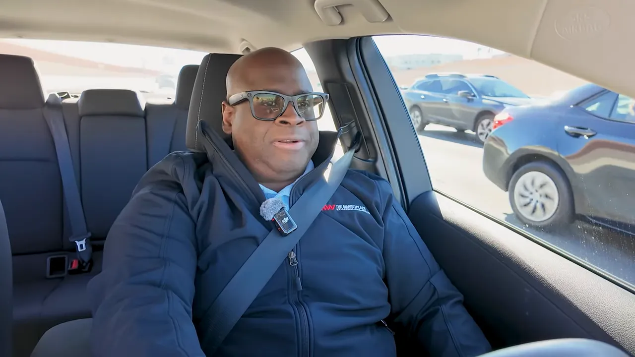 Host in car speaking to camera with passing cars visible outside the window