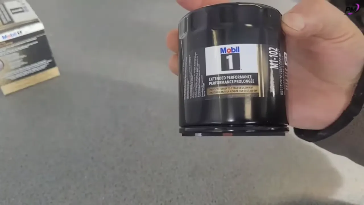 Close-up of a black Mobil 1 oil filter canister (M1-102) with label visible held over a grey surface
