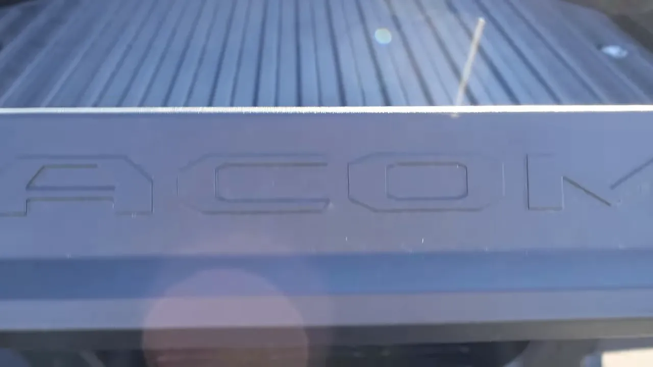 Toyota Tacoma long bed edge with embossed 'TACOMA' on the tailgate and visible bed liner